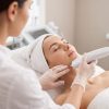 Cosmeticiană aplicând manipulul unui aparat HIFU pe conturul facial al unei cliente